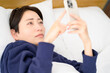 © Yamatatsu - A Japanese woman lying on her back in bed looking at her smartphone and worrying