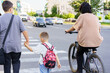 © Nariman - Family crossing the street together on a sunny day while a cyclist passes by in a suburban area