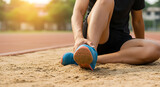Athlete with painful ankle on track. Sport injury during outdoor training. Runner suffering leg pain on sandy field.