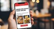 © Izdihaar - A person's hand holds a smartphone displaying a food ordering app.
