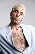 © Studio Marmellata - Trendy young man with multicolored pellets on face and neck looking at camera against gray background