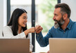 © Peeradontax - A young Asian woman and a mature man with a beard celebrate a success at work with a fist bump.