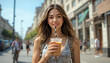 © karp5 - Young Woman Enjoys Cold Beverage in a Lively Urban Street on a Sunny Day While Dressed Casually and Smiling