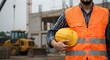 © Javelin - Construction worker in orange safety vest holding yellow hard hat at job site