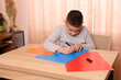 © Vasyl - A boy makes applications from colored paper while sitting at a table. The concept of creativity and leisure.