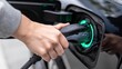© AGI Studio - A close-up of a hand plugging an electric car charger into the vehicle's charging port, highlighted by a green light ring.