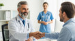 © Kaluya Stock - Patient talking and consultation to senior doctor, shakes hands in a modern clinic, with a female nurse observing in the background