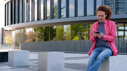 Young redhead man taking selfie and texting on smartphone in modern urban setting