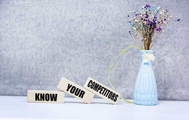 Wall Mural - know your competitors text on wooden blocks on a gray background next to a flower