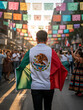© Guillermo - Hombre camina con bandera de México en su espalda por las calles decoradas para la celebración del mes patrio mexicano.