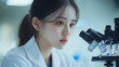© Saba - Woman in lab coat looking into microscope with concentrated expression in a bright laboratory setting