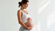 © Khelga Volkova - Pregnant woman smiling while touching her belly against white wall