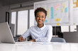 © fizkes - Portrait of smiling African businesswoman, project manager, business analyst or marketing strategist sit at desk in office working on laptop, engaged in planning, coordination tasks, remote workflow