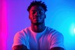 © btiger - Confident young man with relaxed smile wearing white t-shirt illuminated by pink and blue vibrant lighting against a plain background