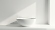 © Sumrit - A single, empty, pristine white bowl sits on a minimalist shelf, bathed in soft, natural light against a stark white backdrop