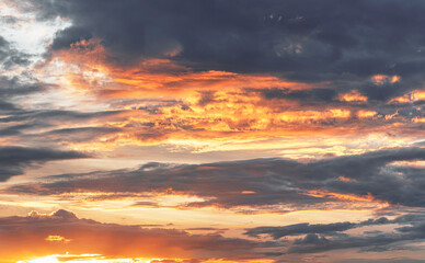 Wall Mural - Dramatic evening sky with glowing orange clouds illuminated by the setting sun against a dark and moody background.