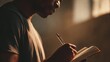 © laperuz - Young Black man writing in notebook during soft natural light