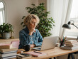 © Alingga - Woman in denim jacket sits focused on laptop in a bright, peaceful home office.