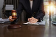 © SOMKID - Lawyer Businesswoman Working with Documents and Signing Contract at Office Desk, Hammer on Wood table, Judge's Gavel, Law, Justice Symbol,