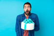 © luismolinero - Young handsome man with a big cake over isolated blue background with surprise facial expression