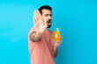 © luismolinero - Young man over holding a cocktail over isolated blue background making stop gesture and disappointed