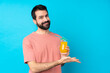 © luismolinero - Young man over holding a cocktail over isolated blue background presenting an idea while looking smiling towards