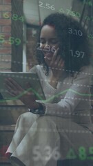 Wall Mural - animation of financial data processing on african american woman having video call on digital tablet
