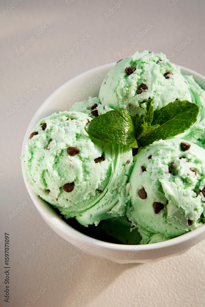 Close-up of creamy mint chocolate chip ice cream scoops in a white bowl, garnished with fresh mint leaves.