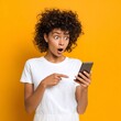 © ryanbagoez - Surprised Young Woman with Curly Hair Using Smartphone Against Bright Yellow Background
