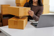 © crizzystudio - Online seller arranging cardboard boxes for delivery using laptop