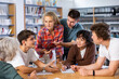 © JackF - Group of fifteen-year-old schoolchildren are preparing for classes in the school library, discussing something and making notes in copybooks