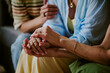 © AnnaStills - Cropped shot of unrecognizable women gently holding hands, showing support and empathy during emotional moment, partial body visible