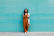 © Westend61 - Smiling person with reusable shopping bag using smartphone by turquoise brick wall