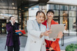 © qunica.com - Professional women engaging in work discussions while utilizing technology outdoors in an urban environment, showcasing teamwork, productivity, and entrepreneurial spirit.