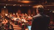 © lail - Speaker addressing a large audience in a theater.