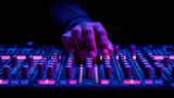 Hand adjusts controls on professional audio mixer, illuminated by vibrant purple and orange lights, creating dynamic atmosphere in music production setting