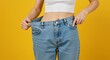 © Arx PhotoStock - Weight loss transformation woman holding oversized jeans against yellow backdrop representing diet and fitness success