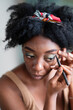 © Studio Marmellata - High angle of focused black female applying eyeliner on eyelid while doing makeup