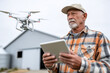 © Anastasiia Havelia - Elderly farmer holding tablet while standing in front of drone station, modern barn in background,