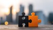 © irul - Two puzzle pieces, black and orange, meet on a wooden surface, cityscape in the background