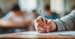 © Marina Demidiuk - Close-up of a hand holding a pen and paper, doing an exam in school, writing something. Blurred background. The student is sitting at their desk, taking a mental test for a final-year class.