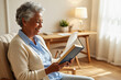 © f_bossa - A smiling senior woman with gray hair sits comfortably in an armchair, engrossed in reading a book.