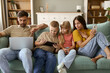 © Goran - Young family using wireless technology while relaxing on sofa in the living room.