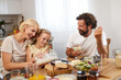 © Stockphotodirectors - A family shares a joyful breakfast at home, with a mother pouring milk, a daughter smiling, and a father holding a bowl. The table is filled with various dishes, creating a warm atmosphere.