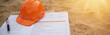 © miss irine - Orange safety helmet and pen rest on checklist paper on sandy construction site. Document details project inspection, safety, quality control, and compliance procedures for building or infrastructure.