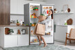© Pixel-Shot - Young businesswoman with bags of food near open fridge in kitchen