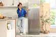 © Pixel-Shot - Young woman talking by mobile phone near fridge in kitchen