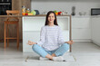 © Pixel-Shot - Young woman meditating on rug in kitchen