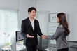 © amnaj - Two asian businesspeople shaking hands after reaching an agreement during a meeting in a modern office with graphs and charts hanging on the wall