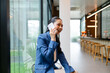 © amnaj - Cheerful young businesswoman in a blue suit is sitting in a modern office cafeteria, taking a break and having a pleasant conversation on her phone